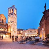 Ferrara  Dick und trutzig sitzt das Castello Estense in seinem Wassergraben in der Mitte der Stadt. Doch da kann sich die mittelalterliche Burg mit ihren Zugbrücken noch so aufspielen – die Hauptrolle in Ferrara spielt, wie überall in der Region Emilia-Romagna, das Essen. Die oberitalienische Stadt feiert besonders ihre Wurstund Aufschnittspezialitäten und ihre Pasta. Fast jedes Restaurant hat die ortstypischen Klassiker auf der Karte: Cappellacci di zucca, mit Kürbispüree gefüllte Nudeln, und Salama da sugo ferrarese, eine weiche, gekochte Salami, die zusammen mit cremigem Kartoffelbrei serviert wird. Eine empfehlenswerte Adresse, um die lokale Küche kennenzulernen, ist etwa die "Osteria i Quattro Angeli" direkt am Castello, hier sitzen mehr Ferraresi als Touristen. Wer sich das viele üppige Essen wieder abtrainieren will, fährt mit dem Fahrrad neun Kilometer entlang der alten Mauern rund um die Stadt, denn Ferrara ist auch eine der Städte mit der höchsten Fahrraddichte der Welt – und das ist eher ungewöhnlich im Vespaland Italien.  Dolcemela: Die komfortable und moderne Pension hat blitzsaubere, hübsche Zimmer und liegt in einer ruhigen Seitengasse im Zentrum. Gutes Frühstück, kostenlose Leihfahrräder. DZ/F ab 80 Euro, www.dolcemela.it