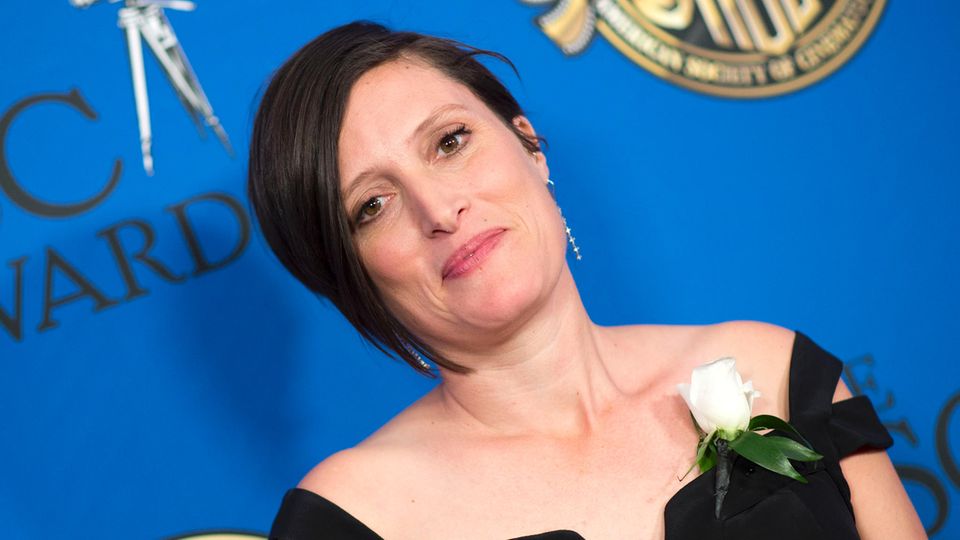 Rachel Morrison Eine weiße Frau mit schwarzem Bob steht im schwarzen, schulterfreien Kleid vor einer blauen Wand.