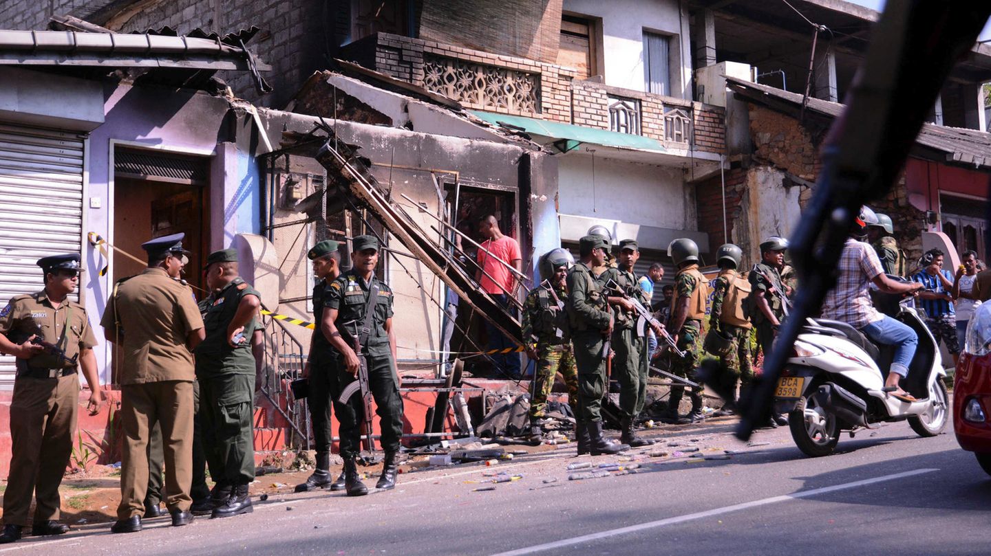 Polizisten und Soldaten stehen in einem Vorort von Kandy, Sri Lanka vor einem verwüsteten Gebäude