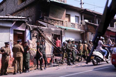 Polizisten und Soldaten stehen in einem Vorort von Kandy, Sri Lanka vor einem verwüsteten Gebäude