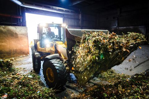 Gelber Bagger in Biogasanlage mit Biomüll auf der Schaufel