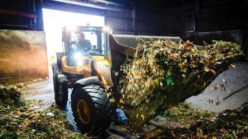 Gelber Bagger in Biogasanlage mit Biomüll auf der Schaufel Gelber Bagger in Biogasanlage mit Biomüll auf der Schaufel