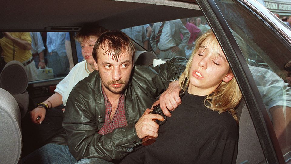 Drei Menschen auf der Rückbank eines Autos: In der Mitte sitzt Dieter Degowski und hält Silke Bischoff eine Waffe an den Kopf