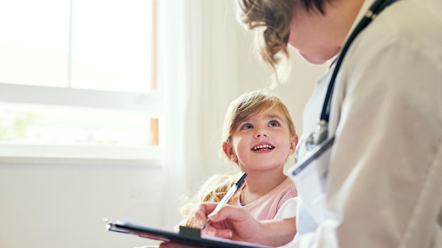 Kind sitzt neben einem Arzt und lächelt