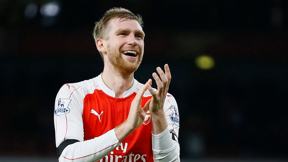 Per Mertesacker Per Mertesacker steht im rot-weißen Arsenal-Trikot nach Abpfiff auf dem Rasen, lächelt und applaudiert.