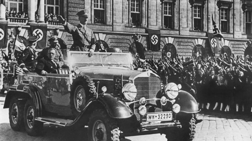 Am 14. März 1938 jubeln Österreicher in Wien Adolf Hitler zu. Neben ihm sitzt der österreichische Kanzler Arthur Seyss-Inquart im Parade-Wagen.