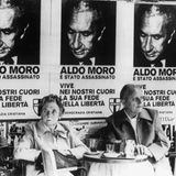 Ein Paar sitzt unter Plakaten mit dem Porträt des ermordeten Aldo Moro
