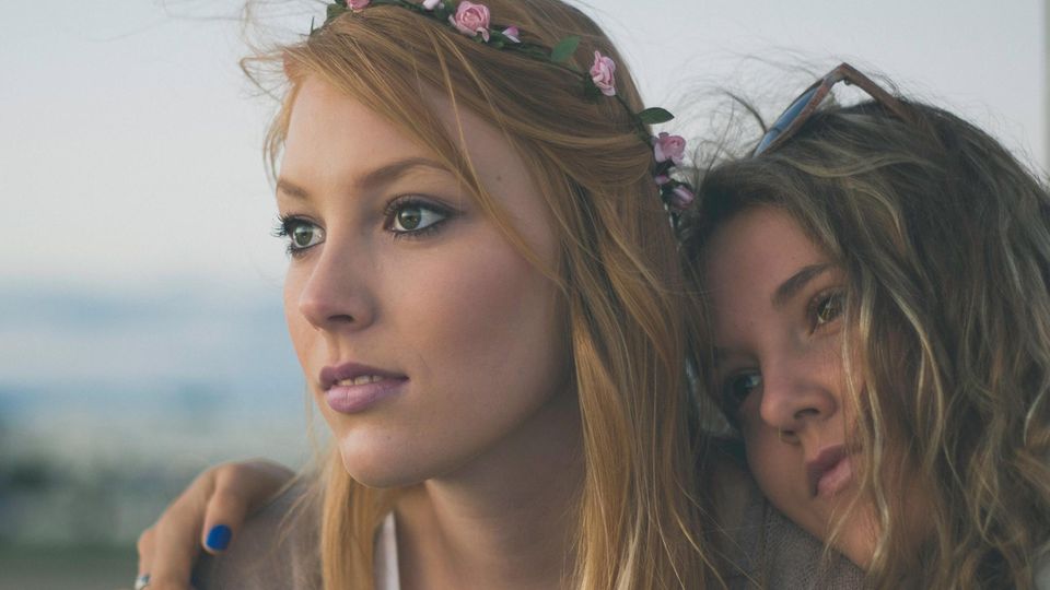 Millennials: Zwei junge Mädchen mit Blumen in den Haaren umarmen sich