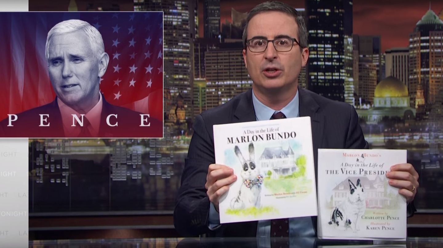 John Oliver sitzt im Anzug in der Kulisse seiner TV-Show und hält zwei fast identische Bücher in die Kamera