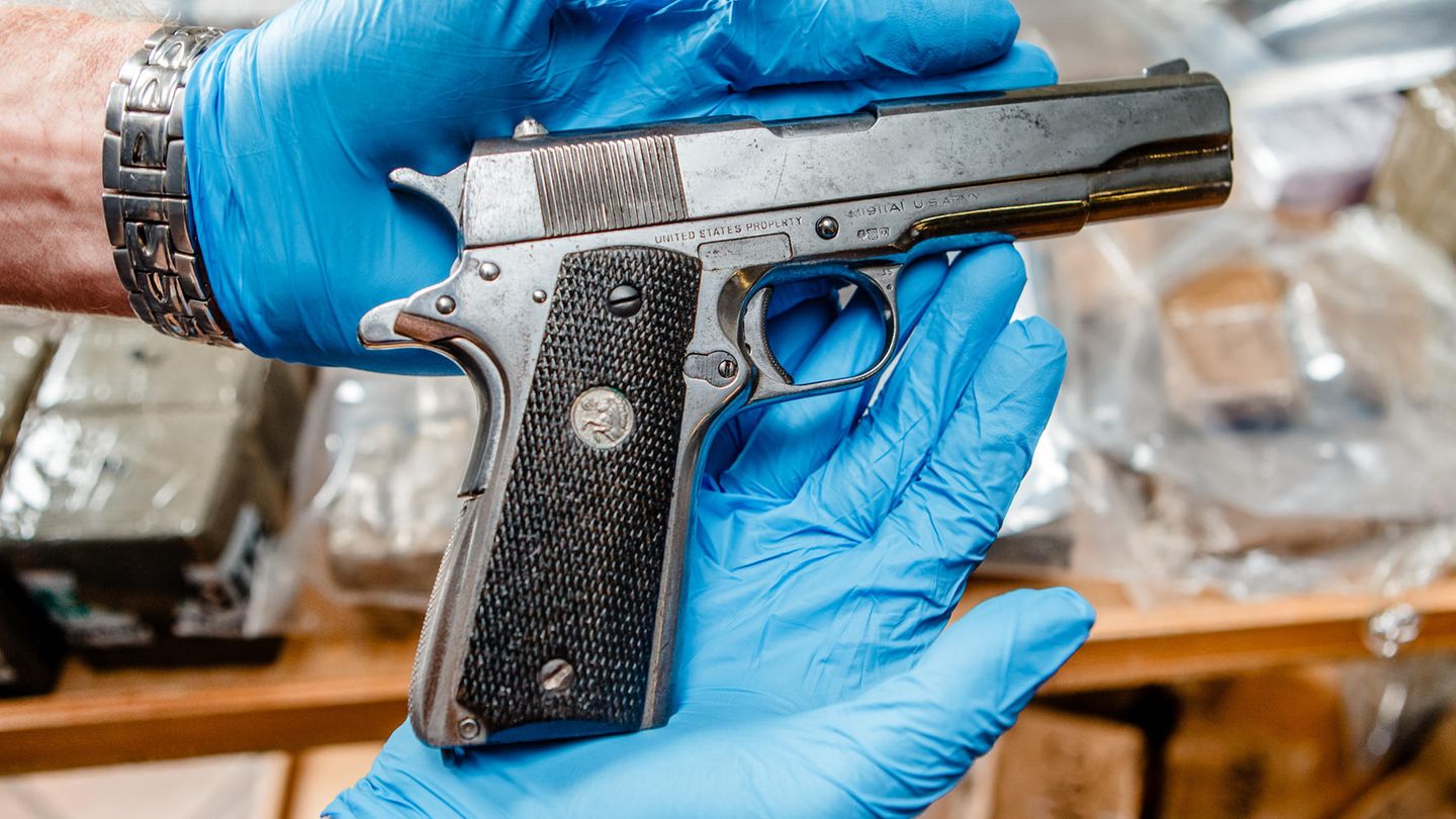 Eine Pistole wird in Händen mit Handschuhen gehalten