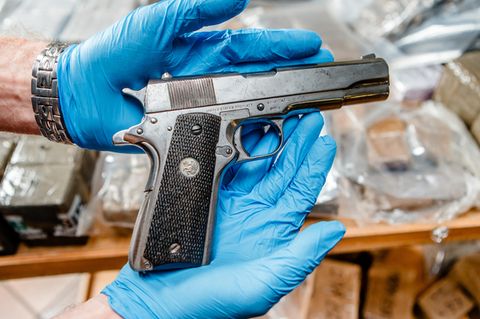 Eine Pistole wird in Händen mit Handschuhen gehalten