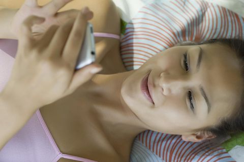 Eine Frau im Bett hält ihr Smartphone in der Hand