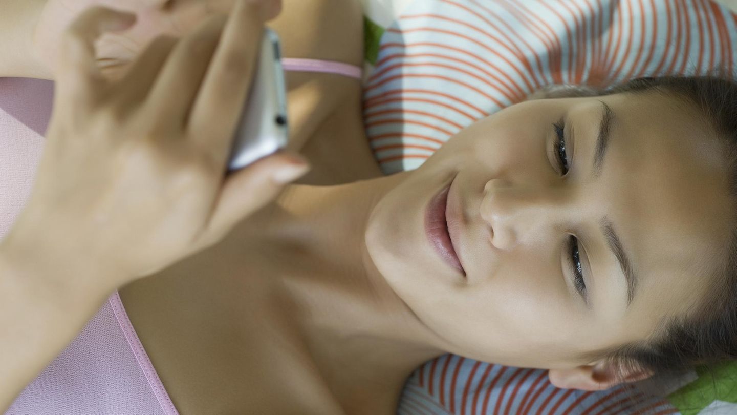 Eine Frau im Bett hält ihr Smartphone in der Hand