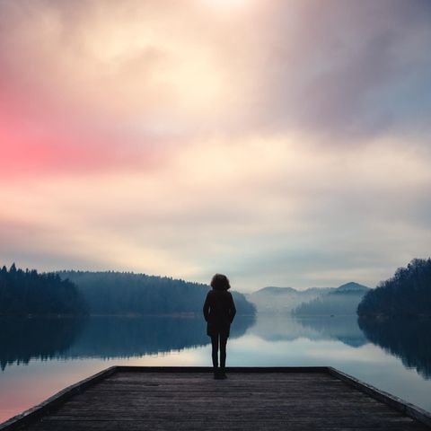 Eine Frau steht an einem See und blickt in die Ferne