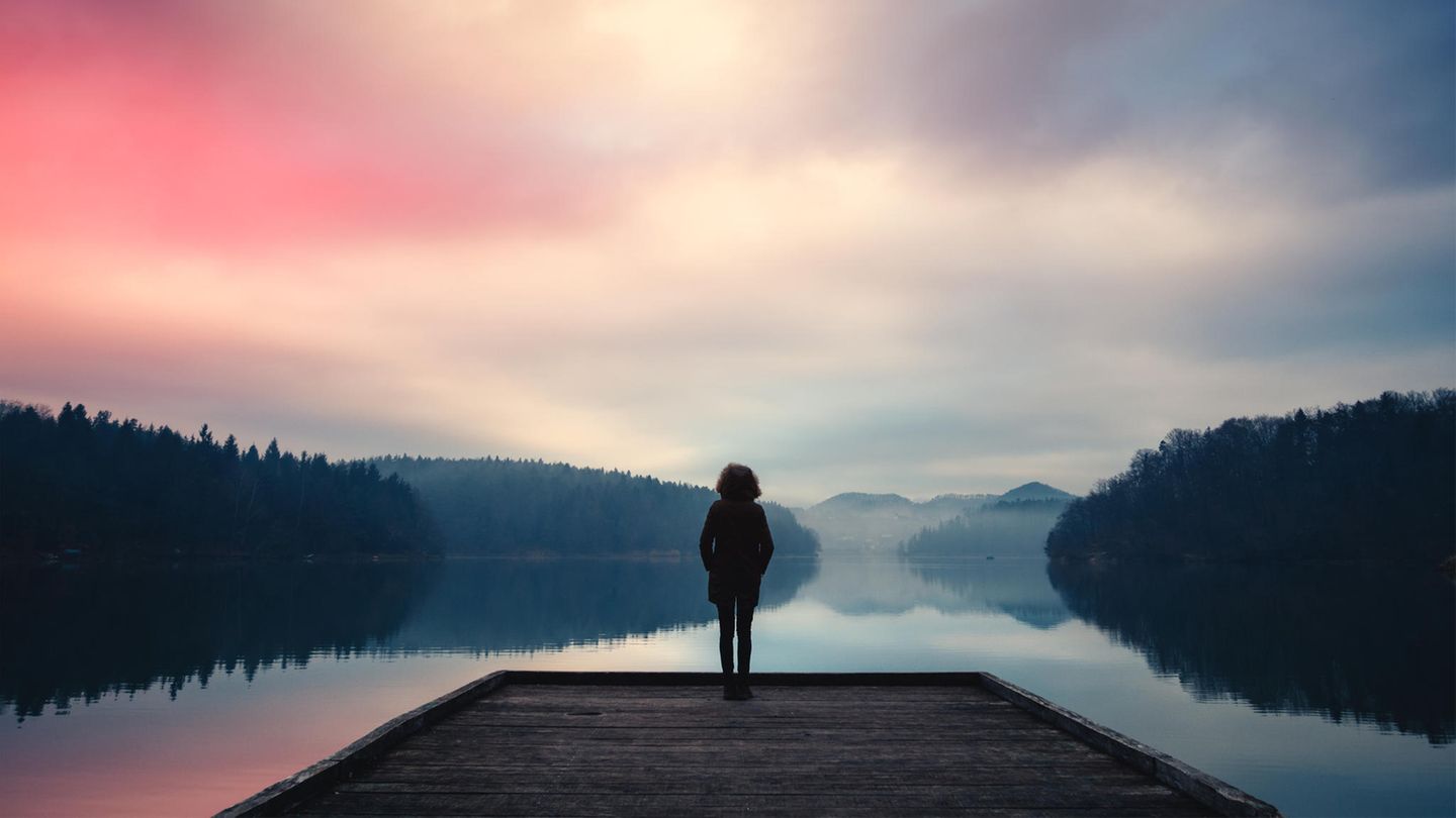Eine Frau steht an einem See und blickt in die Ferne