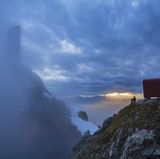 Schutzraum in großer Landschaft – ein Bergsteiger blickt vor dem Bivacco Ugo Dalla Bernardina in der Schiara-Gruppe hinüber zur Turmgestalt der Gusela.