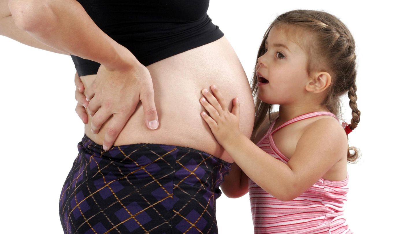 Ein kleines Mädchen spricht mit dem schwangeren Bauch seiner Mutter.