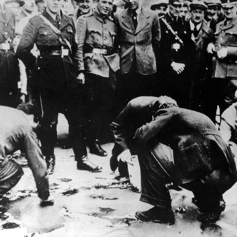 In Wien amüsieren sich Mitglieder der NSDAP über ältere Juden, die den Bürgersteig mit Bürsten schrubben müssen