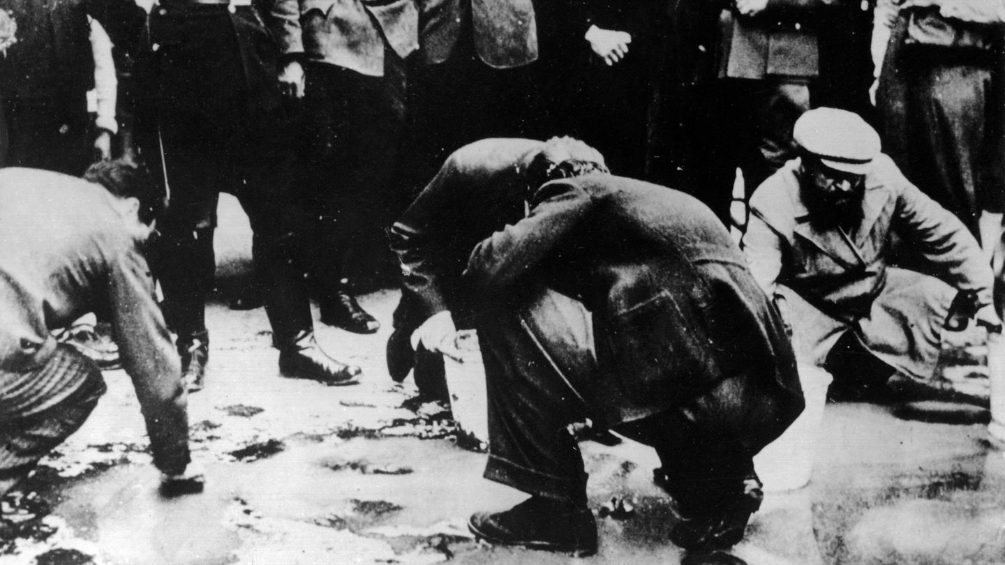 In Wien amüsieren sich Mitglieder der NSDAP über ältere Juden, die den Bürgersteig mit Bürsten schrubben müssen