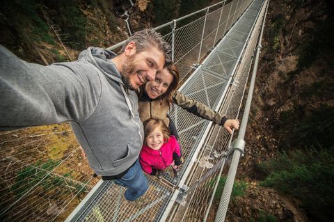 Kleine familiäre Mutprobe  Ein zauberhaftes Tal, ein Wasserfall und dazwischen eine Hängebrücke in gut 60 Metern Höhe. Die schmale, rund 100 Meter lange Brücke im Val di Rabbi ist eine kleine Mutprobe. Wer sie wagt, bekommt eine herrliche Aussicht auf das Tal und den Wasserfall des Rio Ragaiolo. Für Hunde ist der luftige Spaziergang nichts. Die Lauffläche besteht aus Stahlgitter, das die Ballen der Vierbeine verletzen kann.  Vor dem Vergnügen wartet etwas Arbeit: Gute 30 Minuten ist man zu Fuß vom Parkplatz Rabi Fonti unterwegs.