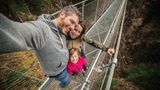 Kleine familiäre Mutprobe  Ein zauberhaftes Tal, ein Wasserfall und dazwischen eine Hängebrücke in gut 60 Metern Höhe. Die schmale, rund 100 Meter lange Brücke im Val di Rabbi ist eine kleine Mutprobe. Wer sie wagt, bekommt eine herrliche Aussicht auf das Tal und den Wasserfall des Rio Ragaiolo. Für Hunde ist der luftige Spaziergang nichts. Die Lauffläche besteht aus Stahlgitter, das die Ballen der Vierbeine verletzen kann.  Vor dem Vergnügen wartet etwas Arbeit: Gute 30 Minuten ist man zu Fuß vom Parkplatz Rabi Fonti unterwegs.