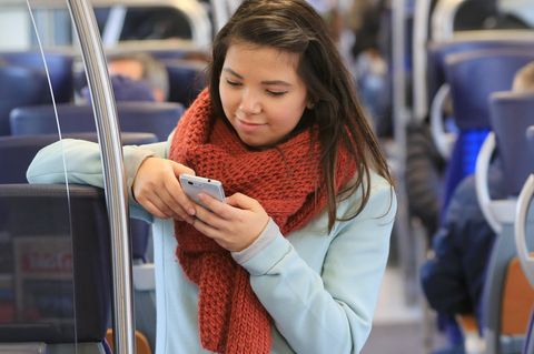 Eine junge Frau tippt in der Bahn auf ihrem Smartphone