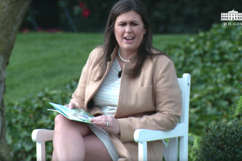 Sarah Huckabee Sanders sitzt auf einem weißen Gartenstuhl im Garten des Weißen Hauses. Auf dem Schoß hat sie ein Kinderbuch.