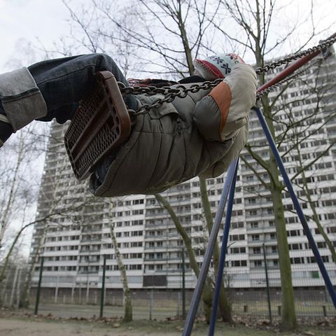 Grundsicherung und Hartz IV in Familien mit Kindern. Ein Kind schaukelt auf einem Spielplatz vor einer Hochhaussiedlung.