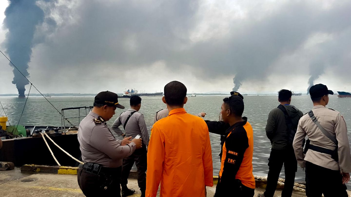 Menschen sehen vom Hafen in Balikpapan, Borneo, auf den Ölteppich im Meer. Rauch steigt auf.