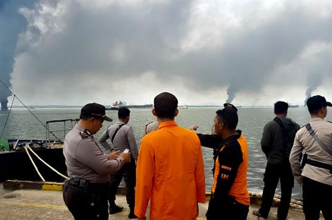 Menschen sehen vom Hafen in Balikpapan, Borneo, auf den Ölteppich im Meer. Rauch steigt auf.