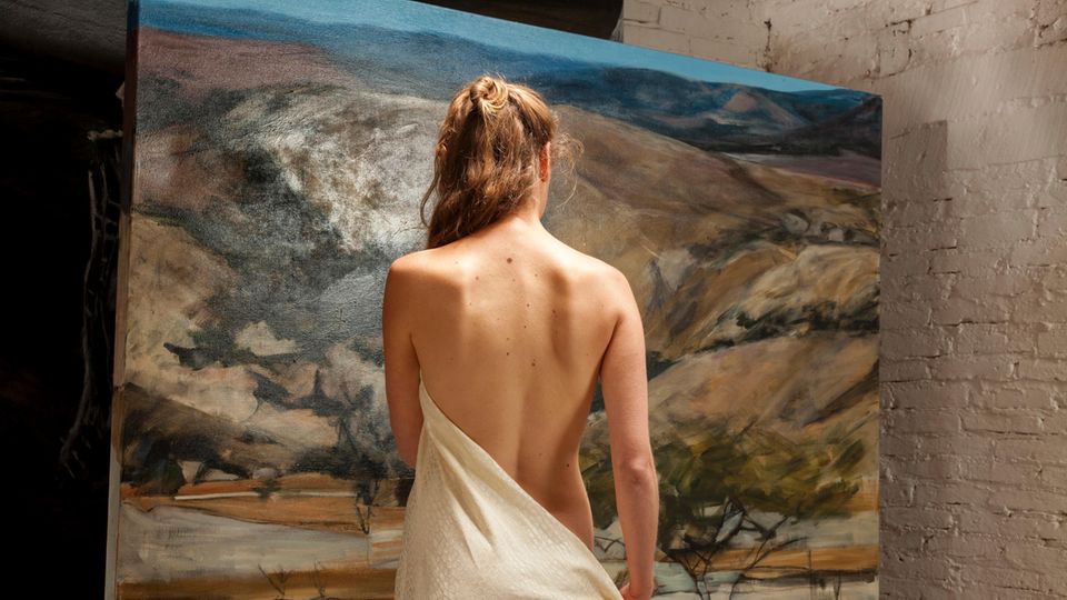 Eine unbekleidete Frau steht vor einem Gemälde