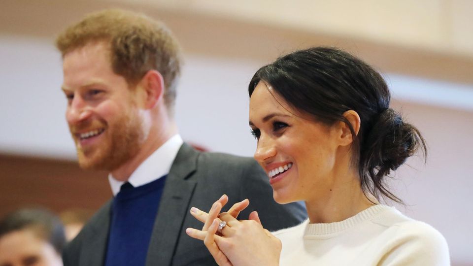 Meghan Markle Prinz Harry Megah Markle steht im weißen Wollpulli neben Prinz Harry und lächelt