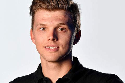Michael Goolaerts, eine junger Mann mit dunkelblondem Seitenscheitel und braunen Augen, steht im schwarzen Team-Shirt im Studio