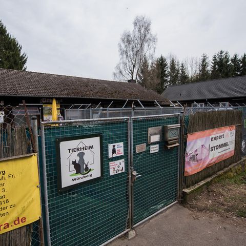 Hinter einem mit Planen verhängten mannshohen Metalltor sind die Dächer zweier Gebäude zu sehen, die im rechten Winkel stehen