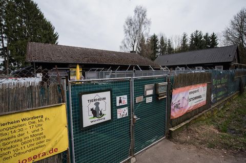 Hinter einem mit Planen verhängten mannshohen Metalltor sind die Dächer zweier Gebäude zu sehen, die im rechten Winkel stehen