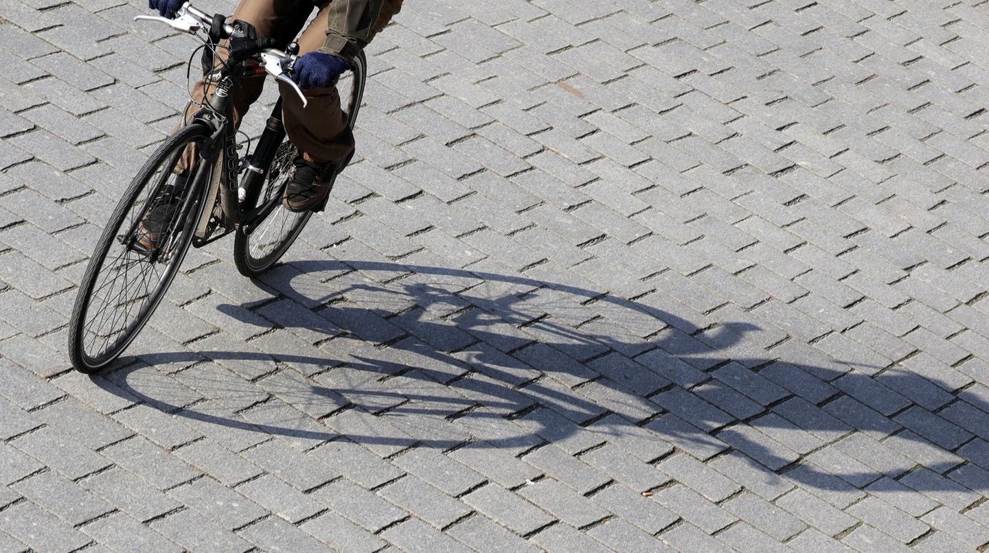 Ein Radfahrer fährt mit Schwung eine Kurve und wirft dabei einen langen Schatten auf graues Straßenpflaster