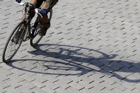 Ein Radfahrer fährt mit Schwung eine Kurve und wirft dabei einen langen Schatten auf graues Straßenpflaster