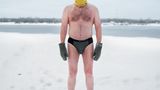 Mann steht in Badekleidung im Schnee