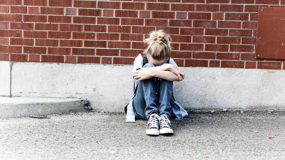 Ein junges Mädchen sitzt vor einer Mauer und weint