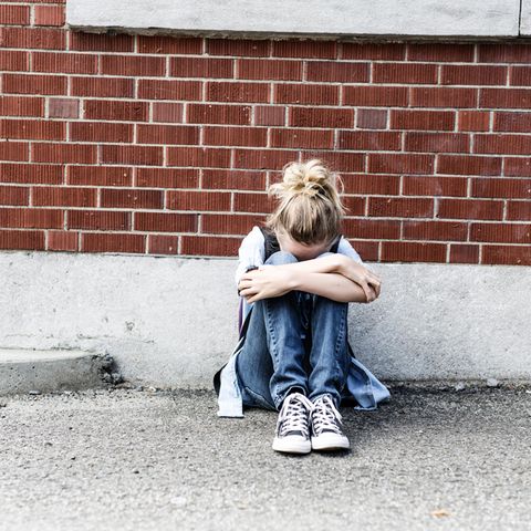 Ein junges Mädchen sitzt vor einer Mauer und weint