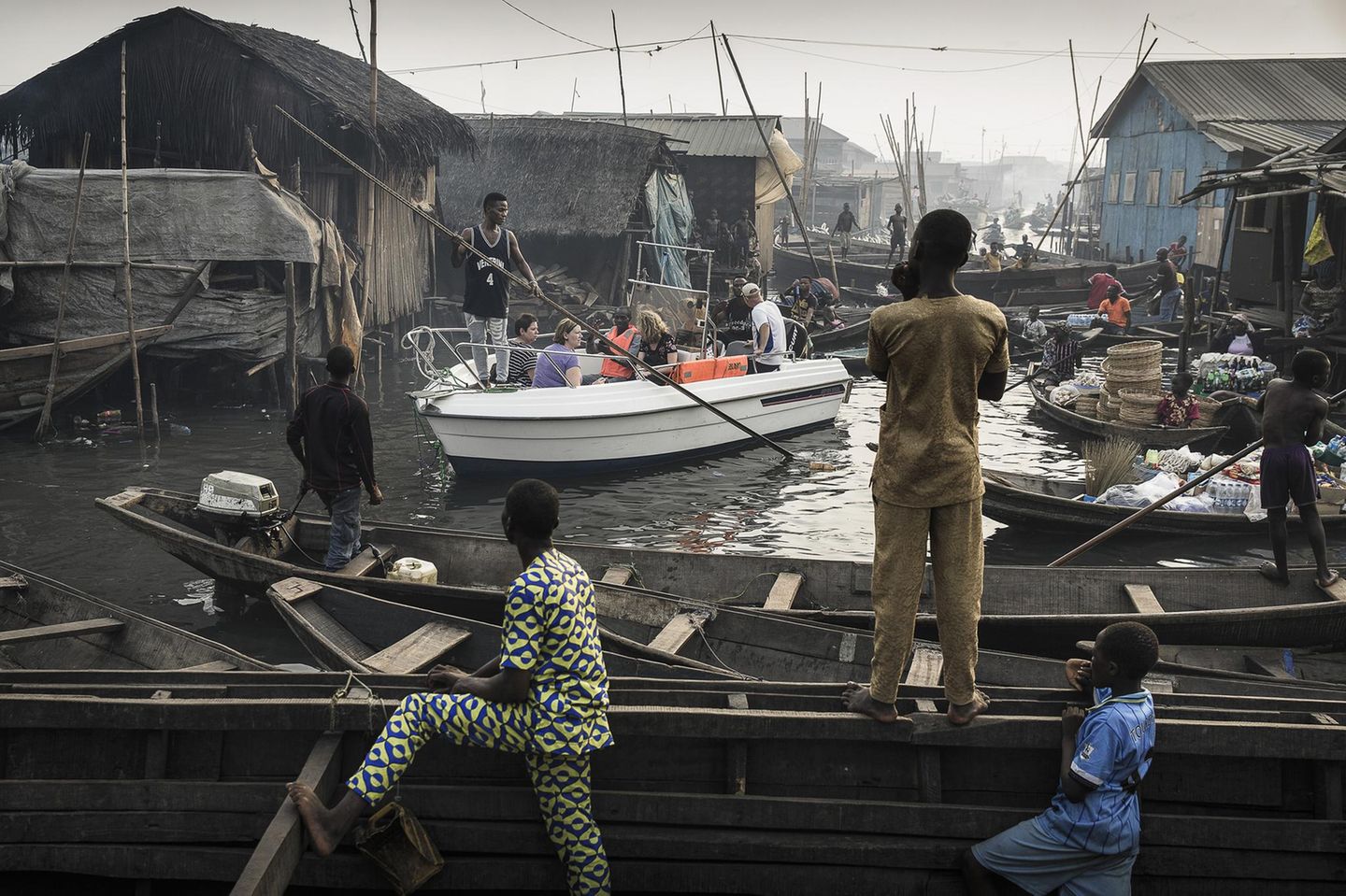 Fotograf: Jesco Denzel    24. Februar 2017    1. Preis im Segment "Einzelfotos"  Ein Boot mit Touristen wird durch die Makoko-Siedlung manövriert. Das frühere Fischerdorf am Ufer der Lagune von Lagos, Nigeria, hat sich zu einem enormen Wasser-Slum entwickelt.    Makoko hat rund 150.000 Einwohner, die meisten Familien leben hier schon seit Generationen. Aber Lagos wächst schnell, da ist Bauland sehr gefragt - und Luxusimmobilien am Ufer der Lagune sind begehrt. Darum versucht man, Gemeinschaften wie Makoko zu vertreiben, damit Apartments gebaut werden können: Wohnungen für die Reichen. Da die Regierung diese Gemeinschaften als informelle Siedlungen betrachtet, dürfen sie geräumt werden, ohne den Einwohnern einen Ersatz anzubieten. Durch die Vertreibung von der "Waterfront" verlieren sie ihre Existenz.