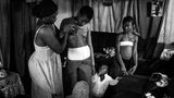 Fotografin: Heba Khamis     6. November - 7. Dezember 2016    1. Preis im Segment "Serien"  In Kamerun ist die Tradition des Brustbügelns verbreitet.  Dabei werden die Brüste junger Mädchen unter Druck mit erhitzten Gegenständen gerieben, um das Wachstum der Brüste zu hemmen oder zu unterdrücken. Man glaubt, dass die Mädchen dadurch langsamer heranreifen und vor Vergewaltigungen oder sexueller Belästigung geschützt werden. Normalerweise wird dies von der Mutter oder einer älteren Verwandten des Mädchens getan. Je nach Region geht man dabei anders vor. Manchmal werden die Brüste mit einem Gurt abgebunden, oder es wird ein erhitzter Mahlstein, Spatel oder Stößel auf die Brüste gedrückt oder gerieben.  Hier massiert Veronica (28) die Brüste ihrer Tochter Michelle (10), ihre anderen Kinder schauen zu.