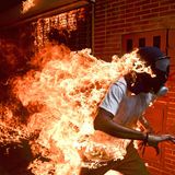 Fotograf: Ronaldo Schemidt     3. Mai 2017    World Press Photo des Jahres     1. Preis im Segment "Einzelfotos"  José Víctor Salazar Balza (28) gerät in Brand bei gewaltsamen Auseinandersetzungen mit der Bereitschaftspolizei, während einer Kundgebung gegen die vom Präsidenten Maduro angekündigte Reform der Staatsordnung, in Caracas, Venezuela.    Maduro wollte das von der Opposition dominierte Parlament durch eine verfassunggebende Versammlung ersetzen und sich damit die gesetzgeberischen Befugnisse faktisch selbst sichern. Oppositionsführer riefen zu Massenprotesten auf, um vorgezogene Präsidentschaftswahlen zu verlangen. Am 3. Mai kam es zu Ausschreitungen zwischen Demonstranten und der Nationalgarde. Die Demonstranten (viele mit Kapuzen, Masken oder Gasmasken) zündeten Brandsätze an und warfen mit Steinen. Balza geriet in Brand, als der Tank eines Motorrads explodierte. Er überlebte mit Verbrennungen ersten und zweiten Grades.