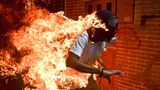 Fotograf: Ronaldo Schemidt     3. Mai 2017    World Press Photo des Jahres     1. Preis im Segment "Einzelfotos"  José Víctor Salazar Balza (28) gerät in Brand bei gewaltsamen Auseinandersetzungen mit der Bereitschaftspolizei, während einer Kundgebung gegen die vom Präsidenten Maduro angekündigte Reform der Staatsordnung, in Caracas, Venezuela.    Maduro wollte das von der Opposition dominierte Parlament durch eine verfassunggebende Versammlung ersetzen und sich damit die gesetzgeberischen Befugnisse faktisch selbst sichern. Oppositionsführer riefen zu Massenprotesten auf, um vorgezogene Präsidentschaftswahlen zu verlangen. Am 3. Mai kam es zu Ausschreitungen zwischen Demonstranten und der Nationalgarde. Die Demonstranten (viele mit Kapuzen, Masken oder Gasmasken) zündeten Brandsätze an und warfen mit Steinen. Balza geriet in Brand, als der Tank eines Motorrads explodierte. Er überlebte mit Verbrennungen ersten und zweiten Grades.