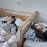 Fotograf: Magnus Wennman     2. März 2017    1. Preis im Segment "Einzelfotos"  Djeneta (rechts) liegt seit zweieinhalb Jahren in komaähnlichem Zustand im Bett, ihre Schwester Ibadeta seit über sechs Monaten. Sie leiden unter uppgivenhetssyndrom (Resignation Syndrome), in Horndal, Schweden.    Djeneta und Ibadeta sind Roma-Flüchtlinge aus dem Kosovo. Am Resignation Syndrome (RS) Erkrankte sind passiv, unbeweglich, stumm, unfähig zu essen und zu trinken, inkontinent und reagieren nicht auf physische Reize. Die Erkrankung scheint nur unter Flüchtlingen in Schweden vorzukommen. Auch wenn die Ursachen rätselhaft sind, halten die meisten Fachleute ein Trauma für einen bedeutenden Auslöser, neben einer Reaktion auf Stress und Depression. Völlig unklar ist auch, warum solche Krankheitsfälle nur in Schweden auftreten. Bisher sind nur Flüchtlingskinder von 7 bis 19 Jahren, hauptsächlich aus der ehemaligen Sowjetunion und dem früheren Jugoslawien, von RS betroffen. Bei vielen trat das Syndrom nach der Ablehnung des Asylantrags auf. Als Heilmittel wird oft vorgeschlagen, den Familien der Erkrankten eine Aufenthaltsgenehmigung zu gewähren.