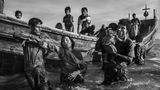 Fotograf: Kevin Frayer     19. September - 2. November 2017    2. Preis im Segment "Serien"  Nach Angriffen auf die Dörfer von Rohingya-Muslimen in Myanmar, bei denen ihre Häuser niedergebrannt wurden, versuchten Hunderttausende zu Fuß oder mit Booten nach Bangladesch zu entkommen, wobei viele umkamen. Nach UNICEF-Angaben waren mehr als 50 Prozent der Flüchtlinge Kinder. In Bangladesch wurden die Flüchtlinge in bestehenden und behelfsmäßigen Lagern untergebracht. Die Bedingungen wurden kritisch; die Grundversorgung geriet in Gefahr, und wie ein Arzt von "Ärzte ohne Grenzen" sagte, drohten Krankheiten durch den Mangel an sauberem Wasser, Unterkünften und sanitären Einrichtungen.    Hier hilft jemand einer Frau aus dem Boot bei ihrer Ankunft in Shah Porir Dwip, nahe Cox’s Bazar in Bangladesch.