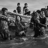 Fotograf: Kevin Frayer     19. September - 2. November 2017    2. Preis im Segment "Serien"  Nach Angriffen auf die Dörfer von Rohingya-Muslimen in Myanmar, bei denen ihre Häuser niedergebrannt wurden, versuchten Hunderttausende zu Fuß oder mit Booten nach Bangladesch zu entkommen, wobei viele umkamen. Nach UNICEF-Angaben waren mehr als 50 Prozent der Flüchtlinge Kinder. In Bangladesch wurden die Flüchtlinge in bestehenden und behelfsmäßigen Lagern untergebracht. Die Bedingungen wurden kritisch; die Grundversorgung geriet in Gefahr, und wie ein Arzt von "Ärzte ohne Grenzen" sagte, drohten Krankheiten durch den Mangel an sauberem Wasser, Unterkünften und sanitären Einrichtungen.    Hier hilft jemand einer Frau aus dem Boot bei ihrer Ankunft in Shah Porir Dwip, nahe Cox’s Bazar in Bangladesch.