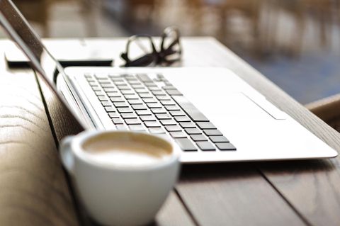 Kaffeetasse vor einem Laptop und einer Brille