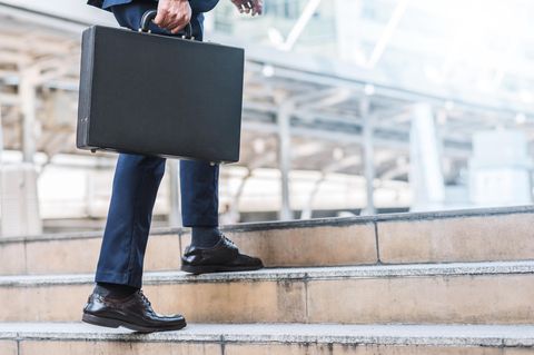 Ein Mann im dunklen Anzug und mit Aktenkoffer steigt eine Treppe empor