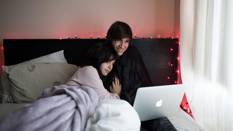 Ein Paar liegt mit Laptop im Bett